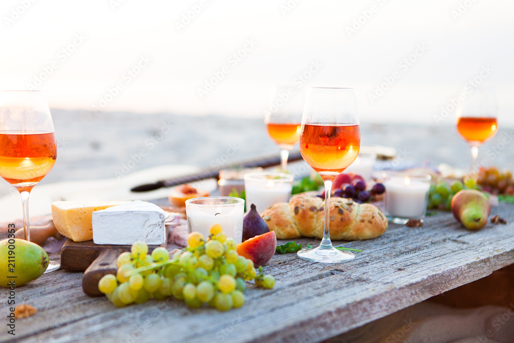 Wall mural Picnic on beach at sunset in boho style. Romantic dinner, friends party, summertime, food and drink concept