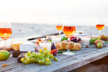 Picnic on beach at sunset in boho style. Romantic dinner, friends party, summertime, food and drink concept