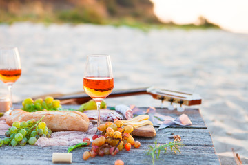 Picnic on beach at sunset in boho style. Romantic dinner, friends party, summertime, food and drink concept