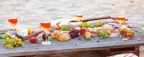 Picnic on beach at sunset in boho style. Romantic dinner, friends party, summertime, food and drink concept - 211900379