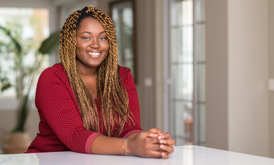 African american woman sitting at home with a happy face standing and smiling with a confident smile showing teeth