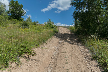 Fototapeta na wymiar A mountain dusty road running along a steep slope, against a backdrop of green trees on either side