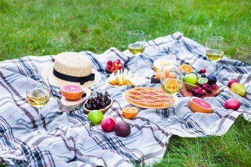 Picnic background with white wine and summer fruits on green grass, summertime party