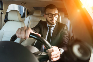 handsome driver in suit and glasses driving auto during sunset