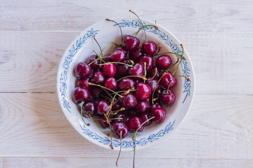 top view of cherry in rustic white plate on wooden table.