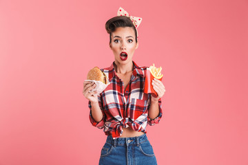 Shocked young pin-up woman holding french fries and burger.
