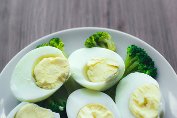 Boiled eggs and broccoli on a white plate on a wooden table.