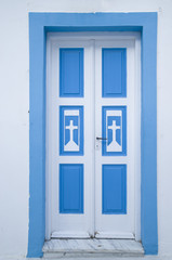 Old blue wooden church door on white wall, Greece