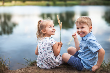 Your Happy Kids, Girl And Boy Are Sitting Near Lake