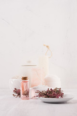 Gentle pink cosmetics oil, small flowers and white soap, cream, clay, towel on white wooden shelf, copy space, vertical.