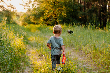 Little boy in summer sunny day holding toy in hands and running. Back view.