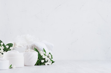 Organic delicate white cosmetics products -  cream, salt, clay, scrub and bath cotton towel, flowers on white wooden background, copy space, interior.