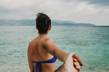 Sweet tourist woman holding hands with her boyfriend in Gili Trawangan island, Indonesia on a beautiful beach with the blue sea backgrounds. Lifestyle. Travel photography.