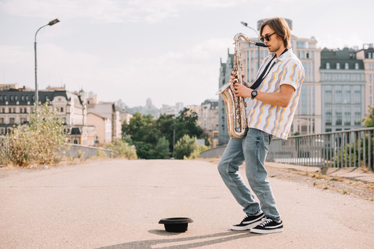 Young happy male busker playing saxophone at city street