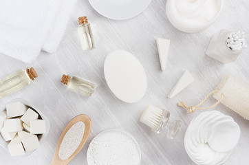 Fototapeta na wymiar Fresh white natural cosmetics - white cream, oil, towel and bath accessories on soft light white wood table, flat lay.