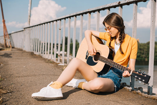 Young woman with guitar sitting on ground and performing on street