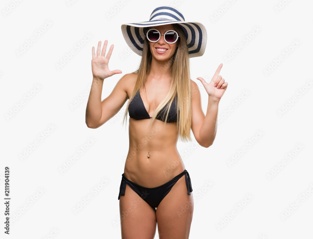 Poster beautiful young woman wearing bikini, sunglasses and hat showing and pointing up with fingers number