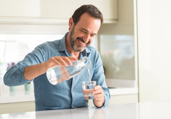 Middle age man drinking a glass of water with a happy face standing and smiling with a confident smile showing teeth - Powered by Adobe
