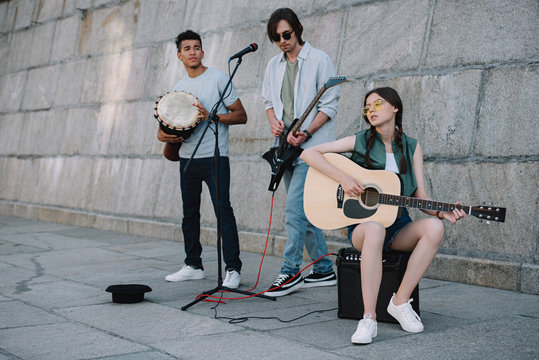 Young girl and multiracial men with musical instruments performing on sunny city street
