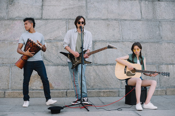 Young and happy street musicians band with guitars and djembe in city