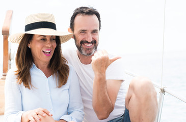 Middle age couple traveling on sailboat pointing with hand and finger up with happy face smiling