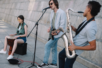 Team of young friends musicians playing and singing in urban environment
