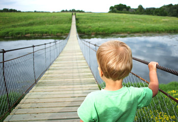 Cute toddler boy on a suspension bridge across the river. Adventure travel, look into the future,...