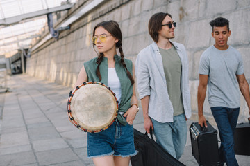 Fototapeta na wymiar Team of young male and female friends walking and carrying musical instruments in urban environment