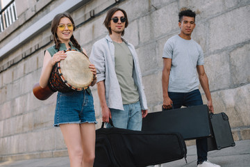 Young girl and multiracial men walking and carrying musical instruments on sunny city street