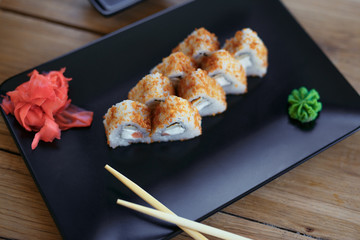 Rolls with chopsticks on the black plate on wooden background with ginger and vassabi