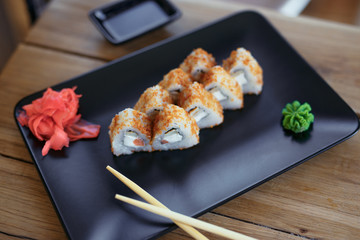 Rolls with chopsticks on the black plate on wooden background with ginger and vassabi