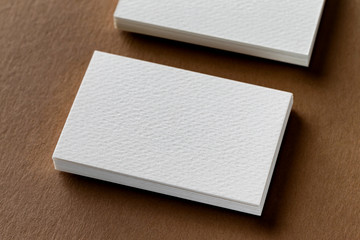 Closeup mockup of two white business cards stacks at brown craft textured paper background.