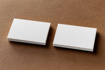 Mockup of two white business cards stacks at textured brown paper background.