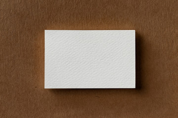 Top view mockup of single white business card at brown craft paper background.