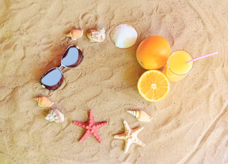 Fototapeta na wymiar Glass of orange juice, oranges, sunglasses, starfishes and seashells on sand beach