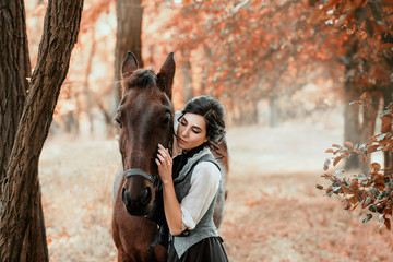 A young lady in a vintage dress, with tenderness and with affection hugs her horse. An ancient, collected hairstyle, a gentle make-up. Gold autumn background. Art photo