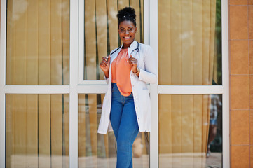 African american doctor female at lab coat with stethoscope posed outdoor against clinic.