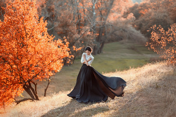The lady in a vintage dress strolls along the picturesque, golden, autumn hills at sunset. A long...