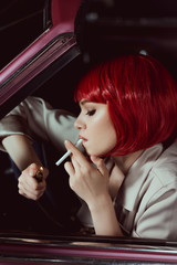 side view of beautiful young woman in red wig smoking cigarette in car