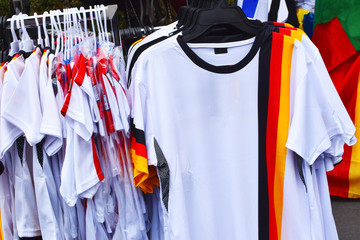 Football fans accessories white t-shirts with colors of german flag stand on street for sale.