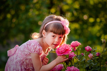 Happy little girl in a pink dress with flowers roses in the nature