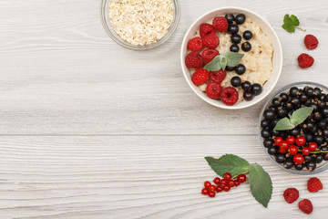 Oatmeal porridge in porcelain bowl with currant berries and raspberries, decorated with mint leaves