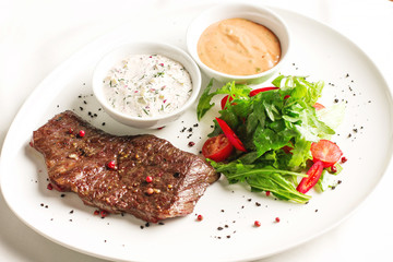 Meat steak beef with fresh vegetables, herbs and two kinds of sauces on white dish