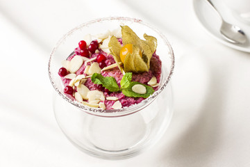 Pink raw dessert mousse ice cream with berries and nuts in glass jar on white table