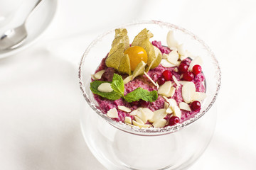 Pink raw dessert mousse ice cream with berries and nuts in glass jar on white table