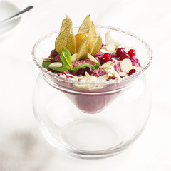 Pink raw dessert mousse ice cream with berries and nuts in glass jar on white table