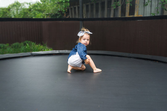 Active barefoot baby girl plays outdoors in playground. Portrait of the little girl on a trampoline