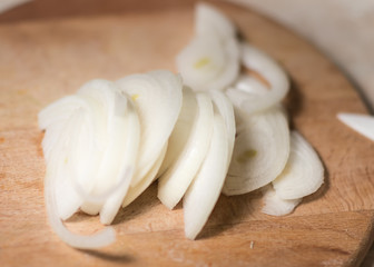 Onion and onion slices on wooden cutting board.