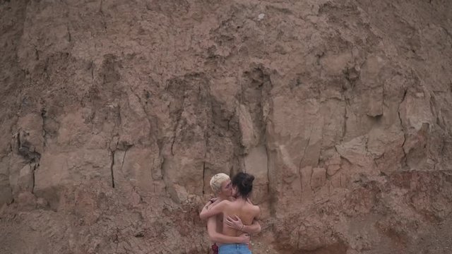 Topless couple kissing outdoor near wall.
