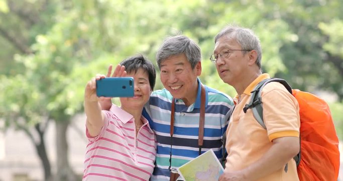 Senior friends go a trip together at outdoor and take selfie by mobile phone